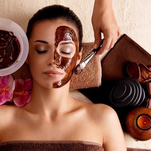 Therapist applying a cacao facial mask by candlelight